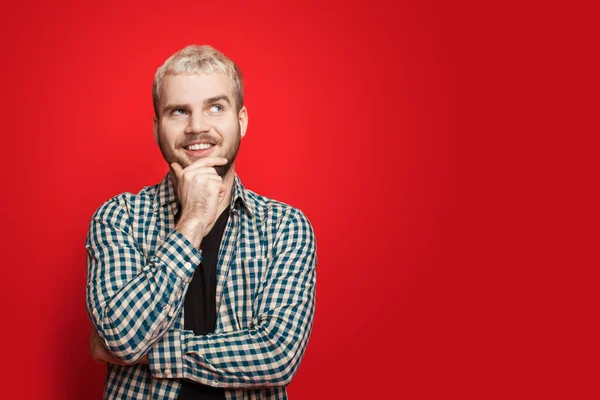 Homem caucasiano que teve a ideia e está posando de lado em uma parede de estúdio vermelho com espaço livre tocando seu queixo e sorriso — Fotografia de Stock