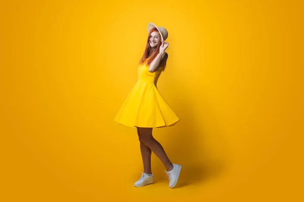 Монохромне фото імбирної леді з капелюхом на голові і жовтим платтям, що позує на стіні студії — стокове фото