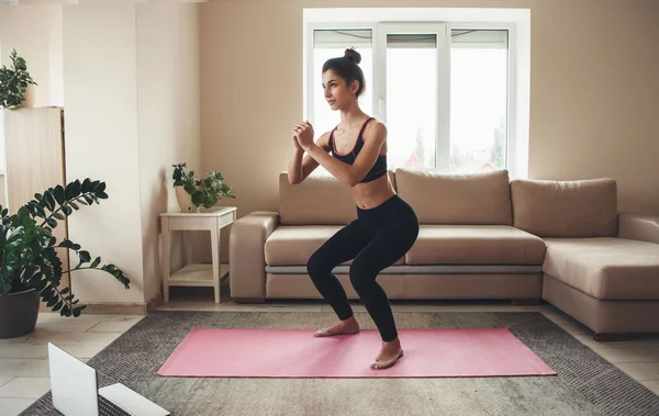 穿着运动服的胖女人在家里用笔记本电脑在瑜伽地毯上锻炼腿 — 图库照片