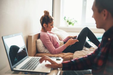 Bilgisayarın başında birlikte çalışan beyaz bir çiftin yan görüntüsü ve telefon kullanarak gülümsemesi.