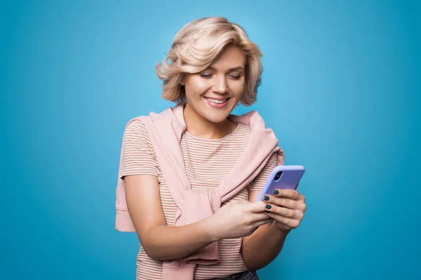 Caucasian woman chatting on mobile and smile cheerfully on a blue studio wall