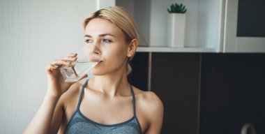Yoga egzersizlerinden sonra mutfakta spor giyerek su içen genç bayan.