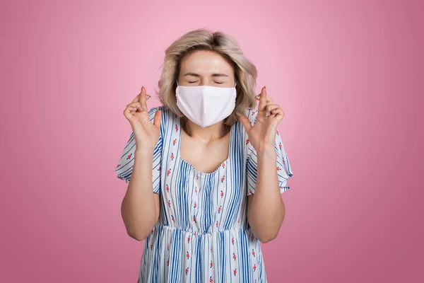 Charmante blonde Dame im Sommerkleid mit medizinischer Maske auf dem Gesicht gestikuliert einen Traum auf einer rosa Studiowand — Stockfoto