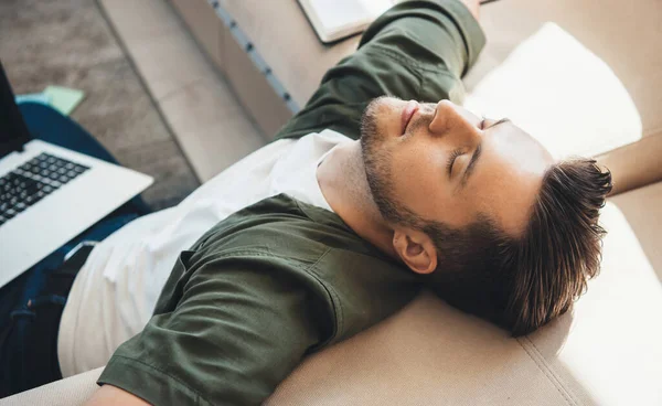 Foto vista superior de um homem cansado deitado perto do sofá no chão com um laptop depois de trabalhar com olhos fechados — Fotografia de Stock