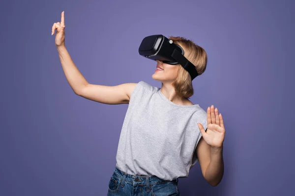 Mulher loira com fone de ouvido vr tocando algo em uma parede de estúdio violeta — Fotografia de Stock