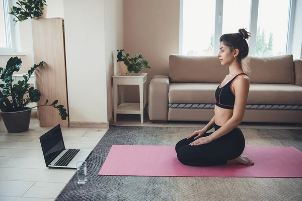 Lección de meditación en el suelo de una morena vestida con ropa deportiva usando un ordenador y un vaso con agua —  Fotos de Stock