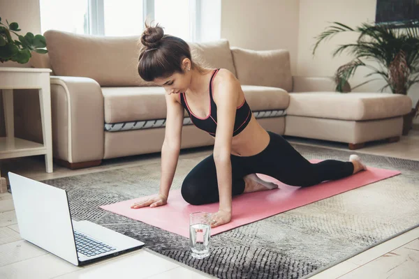 Foto vista laterale di una signora caucasica che fa yoga sul pavimento indossando abbigliamento sportivo e utilizzando il computer portatile con un bicchiere d'acqua — Foto Stock