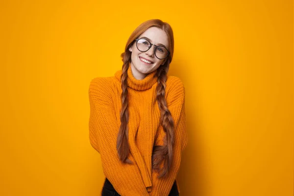 Foto monocromatica di una signora zenzero con lentiggini che indossa un maglione sorride alla fotocamera su un muro di studio giallo — Foto Stock