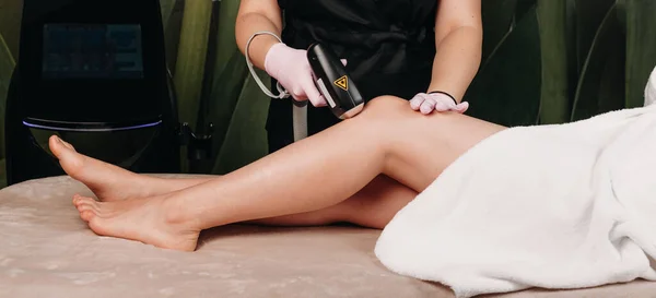 Sesja depilacji nóg laserem przy użyciu nowoczesnego aparatu dla młodej kobiety w centrum spa — Zdjęcie stockowe