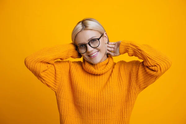 Dulce retrato monocromático de una mujer rubia con anteojos y un suéter naranja cálido sonríe a la cámara en una pared de estudio — Foto de Stock