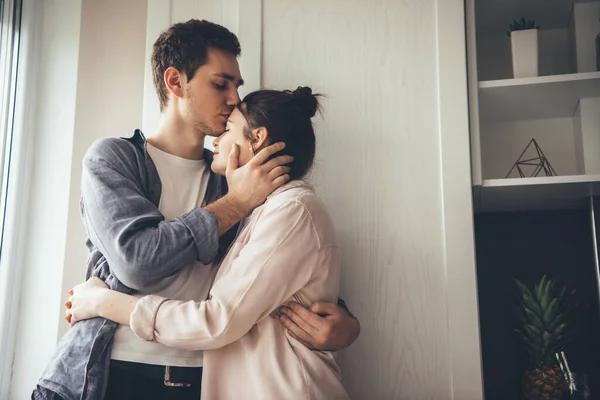 Aranyos fiatal pár csókolózik a konyhában, és ölelkeznek az ablak közelében — Stock Fotó