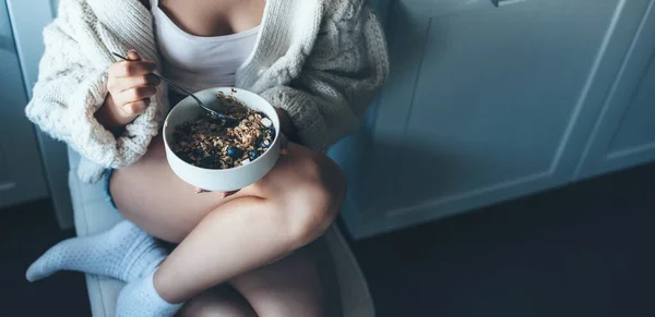 Foto vista superior de una mujer caucásica sentada en el suelo en la cocina y comiendo cereales con un suéter de punto blanco — Foto de Stock