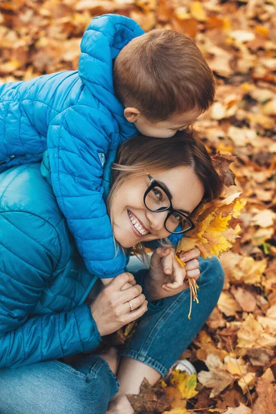 Mavi elbiseli beyaz bir anne ve oğulun parkta sonbahar yürüyüşü sırasında yapraklarla oynadığı üst manzara fotoğrafı. — Stok fotoğraf