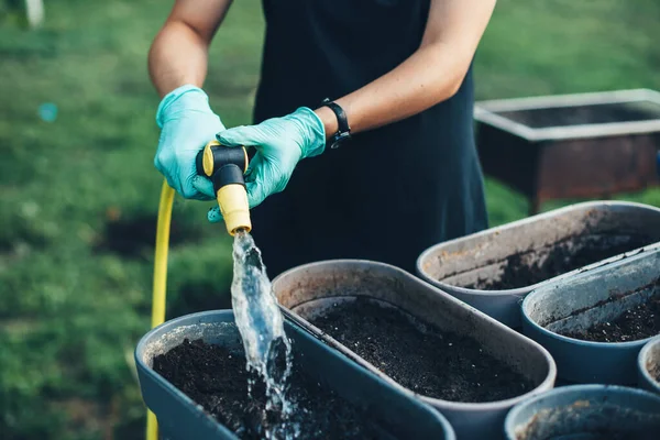 Mulher branca regando vasos com sementes em casa no jardim depois de plantar algo em um dia de verão — Fotografia de Stock