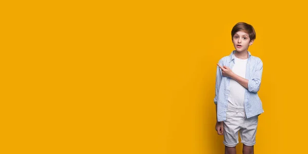 Menino caucasiano jovem vestindo uma camisa está posando surpreso em uma parede de estúdio amarelo com espaço livre apontando para algo com indicador — Fotografia de Stock