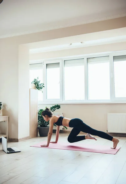 Fitness digitale a casa fatto da una giovane donna sportiva che indossa abbigliamento sportivo utilizzando un computer portatile e facendo tavola — Foto Stock