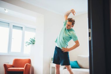 Beyaz adam oturma odasında spor giysisi giymeden önce ısınıp ısınıyor.