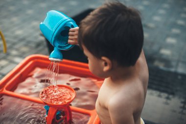 Beyaz çocuk bir yaz günü dışarıda çıplak oynarken oyuncağı suluyor.