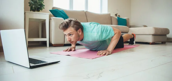 Uomo caucasico che fa flessioni a casa sul pavimento mentre utilizza un computer portatile che fa palestra a casa — Foto Stock