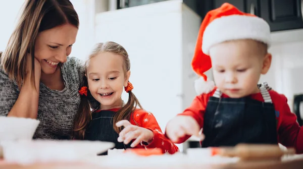 Madre caucasica e i suoi figli vestiti con vestiti da Babbo Natale che cucinano e cuociono biscotti per Natale — Foto Stock