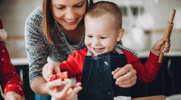 Madre caucásica ayudando a su hijo a enrollar la masa mientras se prepara para las vacaciones de Navidad — Foto de Stock