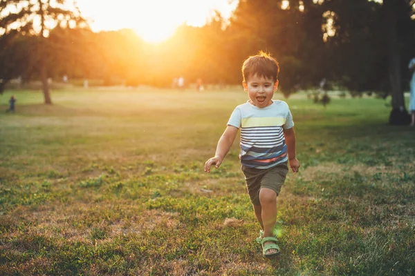 Счастливый маленький мальчик, бегущий в парке перед камерой во время заката летом — стоковое фото