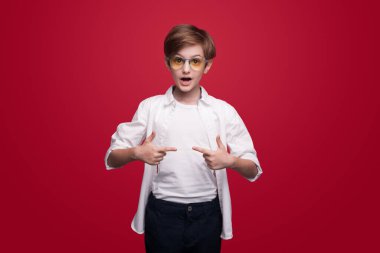 Kırmızı bir stüdyo duvarında gözlük takarken kendini gösteren beyaz çocuk şaşırdı.