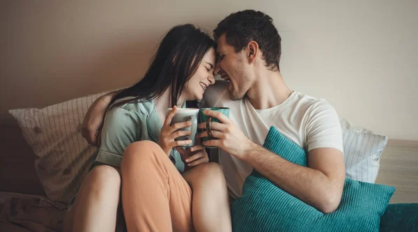 Feliz casal caucasiano sorrir e beber café juntos na cama de manhã abraçando uns aos outros — Fotografia de Stock