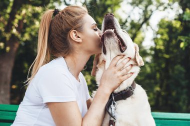 Beyaz bir kadının yaz yürüyüşü sırasında labradorunu öperken çekilmiş yakın bir fotoğrafı.
