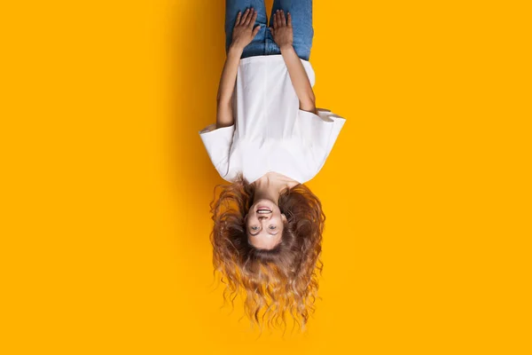 Upside-down photo of a blonde lady in jeans and white t-shirt smiling at camera and advertising something
