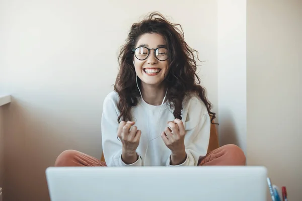 Brunett lockigt hår kvinna gestikulerar lycka och ja tecken under online lektioner med bärbar dator och hörlurar — Stockfoto