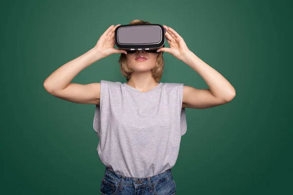 Blonde sviluppatore vr sta utilizzando un auricolare per testare la nuova esperienza su un muro verde in studio — Foto Stock