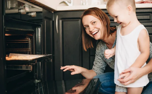 Mãe caucasiana feliz e seu filho fazendo alguns bolos deliciosos estão colocando a massa no forno — Fotografia de Stock