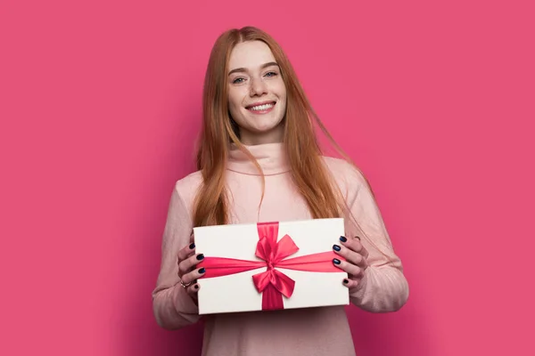 Mujer caucásica con el pelo rojo y pecas se muestra en la cámara actual caja bien lleno posando y sonreír en una pared roja — Foto de Stock