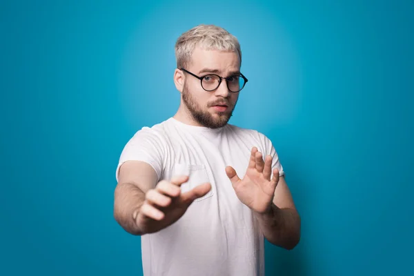 Homem loiro com barba e óculos está gesticulando medo com palmas posando em uma parede azul estúdio — Fotografia de Stock