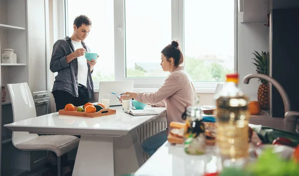 Kaukázusi pár eszik a konyhában, miközben online dolgozik egy laptop és néhány könyvet — Stock Fotó