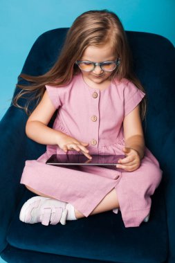 Stüdyoda koltukta otururken tablet kullanan gözlüklü beyaz bir kızın fotoğrafını çek.