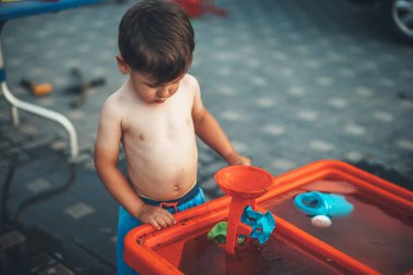 Yakışıklı çıplak çocuk, çocuk gününde bahçede su oyuncaklarıyla oynuyor.