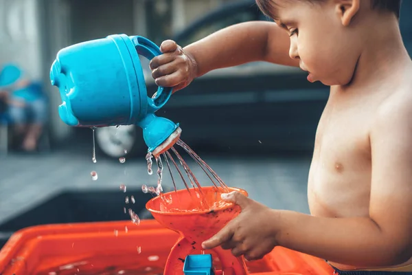 Evde plastik oyuncaklar ve suyla oynayan beyaz bir çocuğun yan görüntüsü.