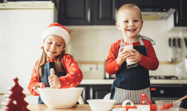 Felice fastidio e sorella cucinare qualcosa in cucina mentre si preparano per le vacanze di Natale indossando vestiti di Babbo Natale — Foto Stock