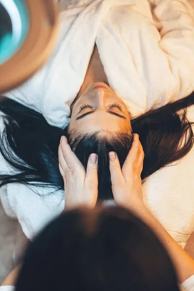 Foto vista superior de una mujer morena tumbada en el salón de spa con un procedimiento de masaje en la cabeza — Foto de Stock