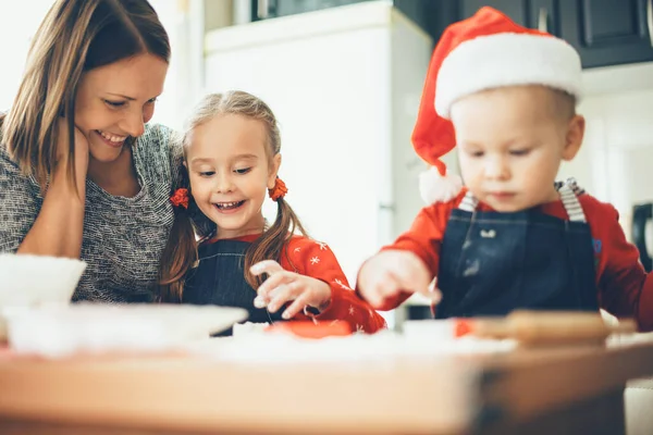Madre caucásica y sus hijos se preparan para las vacaciones de Navidad con ropa de sant y comida para cocinar — Foto de Stock