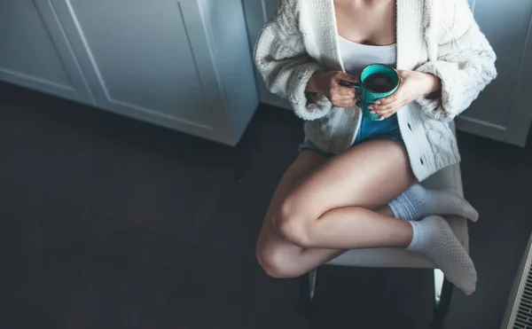 Běloška sedící v křesle v kuchyni a popíjející kávu v pleteném bílém svetru — Stock fotografie
