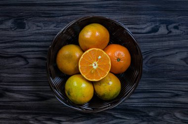 Ahşap masa üzerinde kahverengi hasır sepet içinde dilimlenmiş portakal.