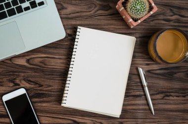 Kahverengi ahşap masa üzerinde bir kitap, kalem, kaktüs ve telefon var..