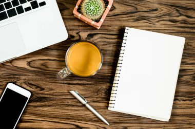 Kahverengi ahşap masa üzerinde bir kitap, kalem, kaktüs ve telefon var..