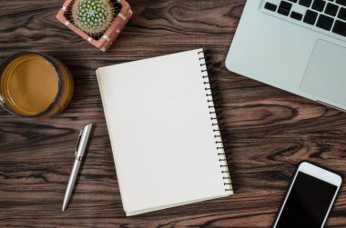 Kahverengi ahşap masa üzerinde bir kitap, kalem, kaktüs ve telefon var..