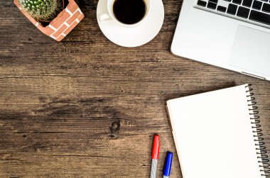 Kahverengi ahşap masa üzerinde bir kitap, kalem, kaktüs ve telefon var..