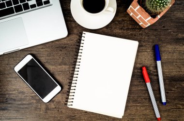 Kahverengi ahşap masa üzerinde bir kitap, kalem, kaktüs ve telefon var..