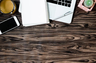 Kahverengi ahşap masa üzerinde bir kitap, kalem, kaktüs ve telefon var..